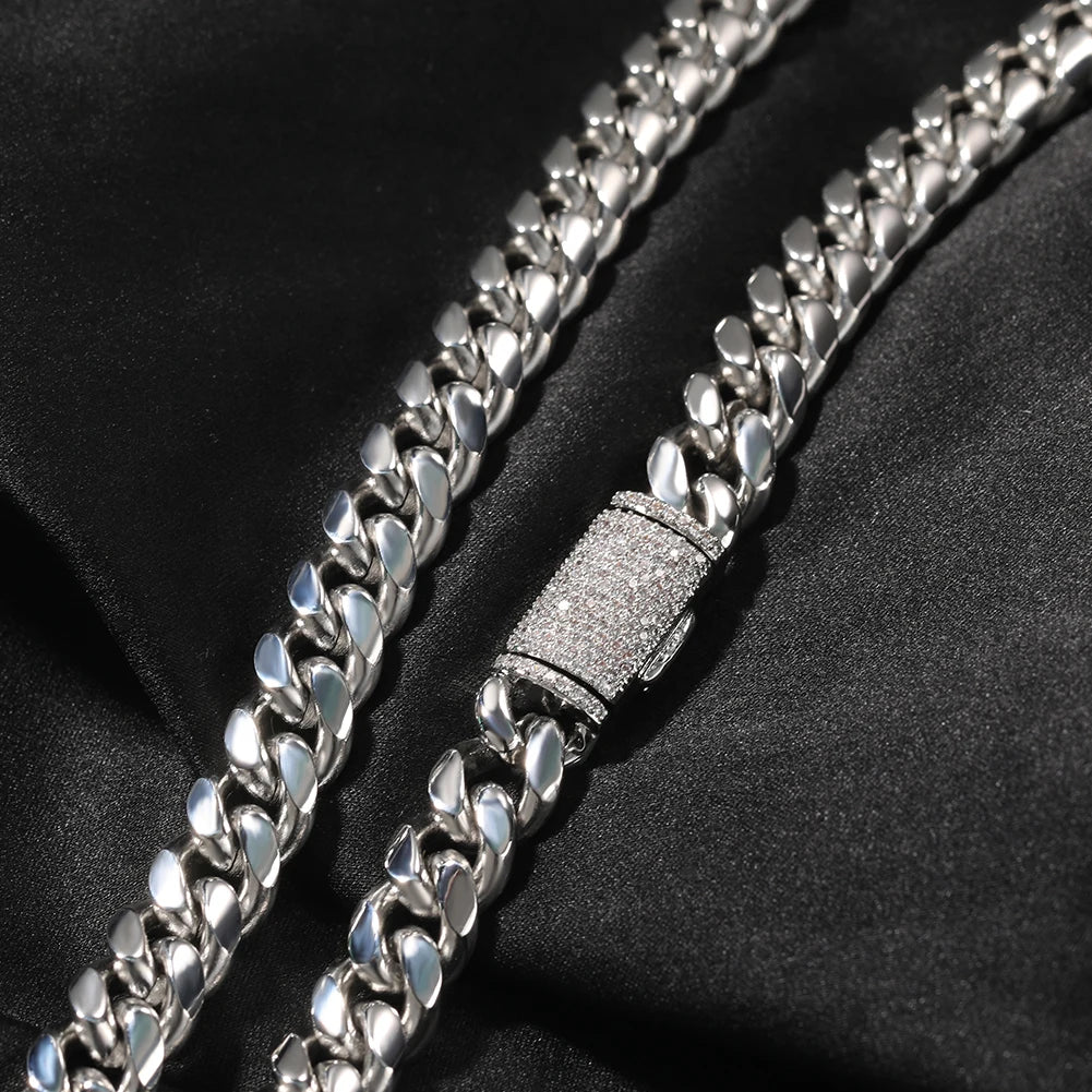 A close-up of a silver stainless steel Cuban link necklace lying on a black fabric.