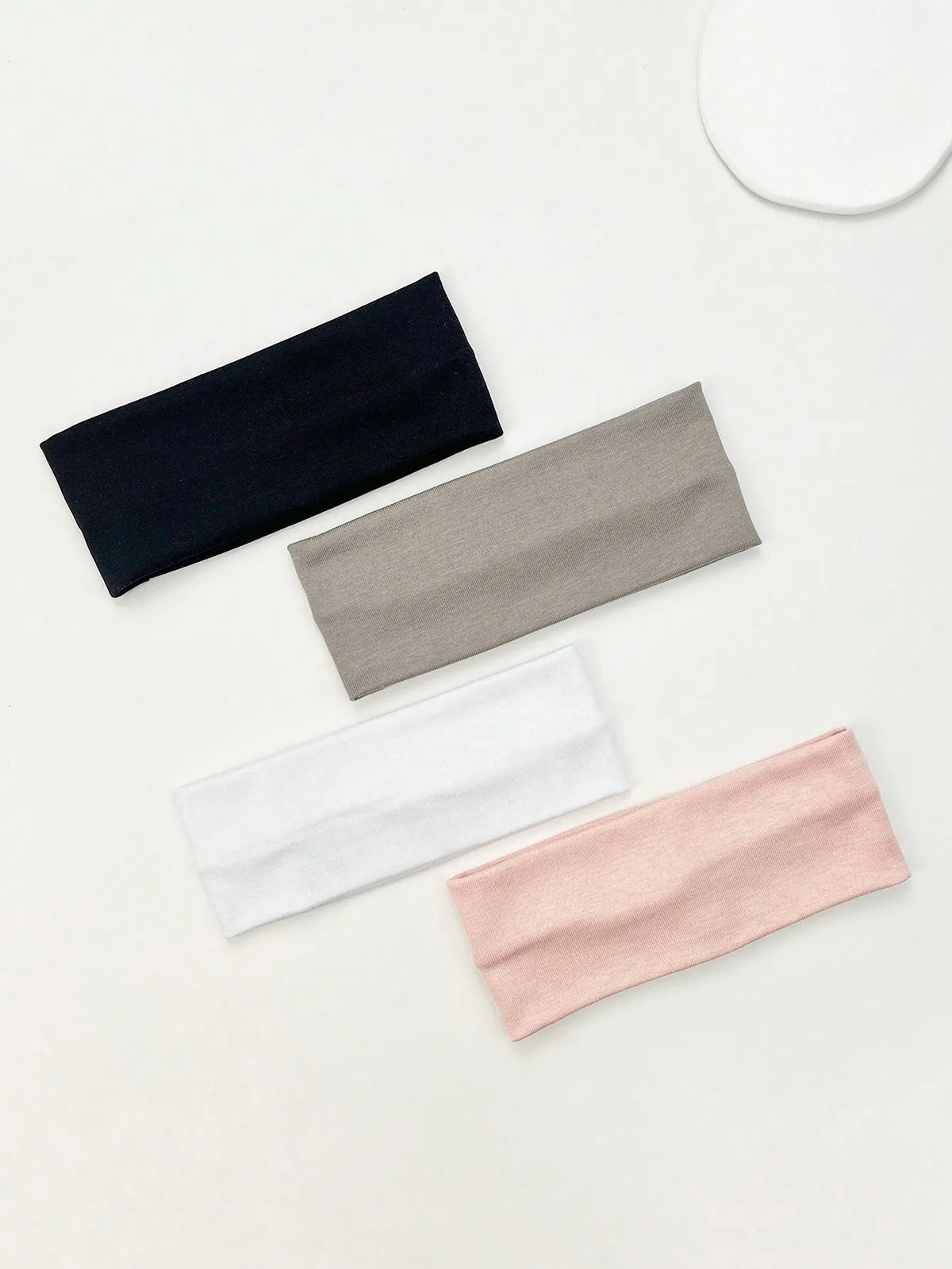 A set of four knitted hair bands in navy blue, gray, white, and pink laid diagonally on a light surface.