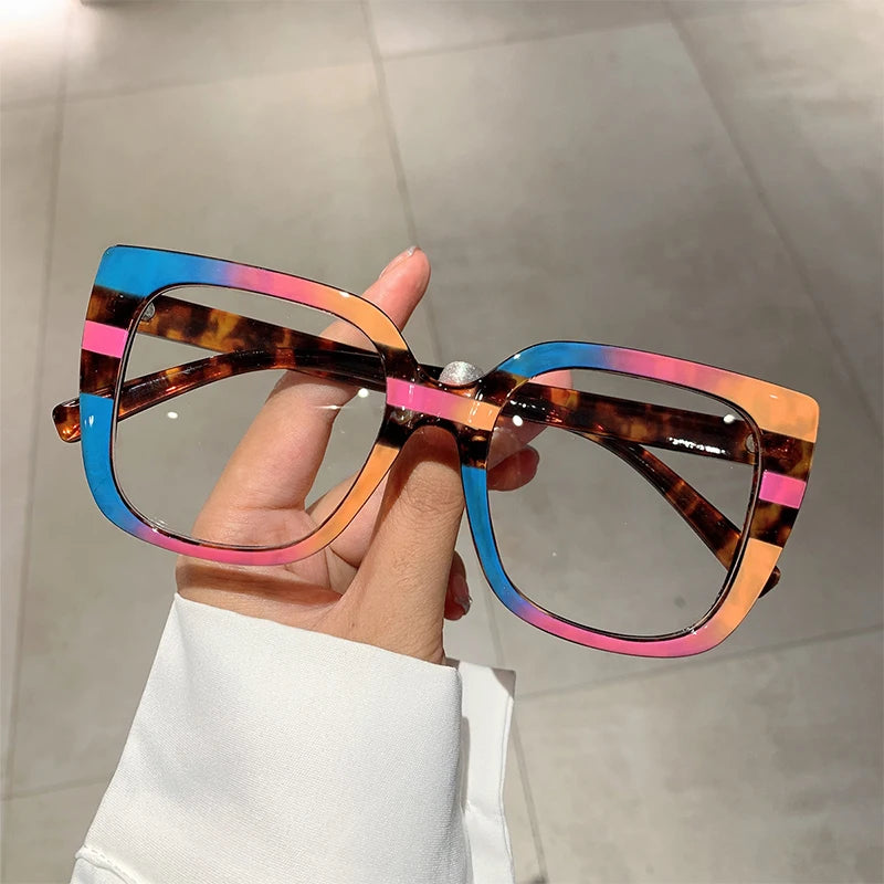 Eine Hand hält eine trendige, große, quadratische Brille mit mehrfarbigen marmorierten Linsen.