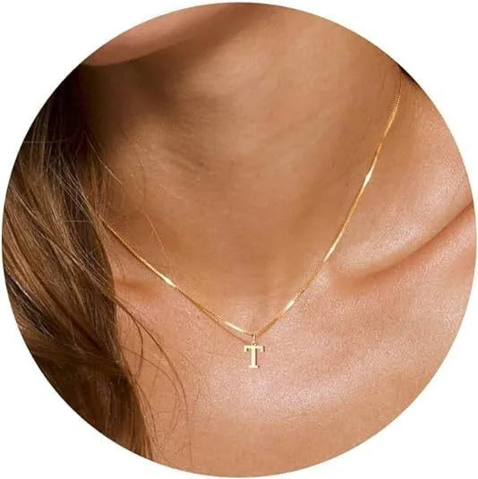 A close-up of a gold plated alphabet initial necklace resting on a person's neck and collarbone.