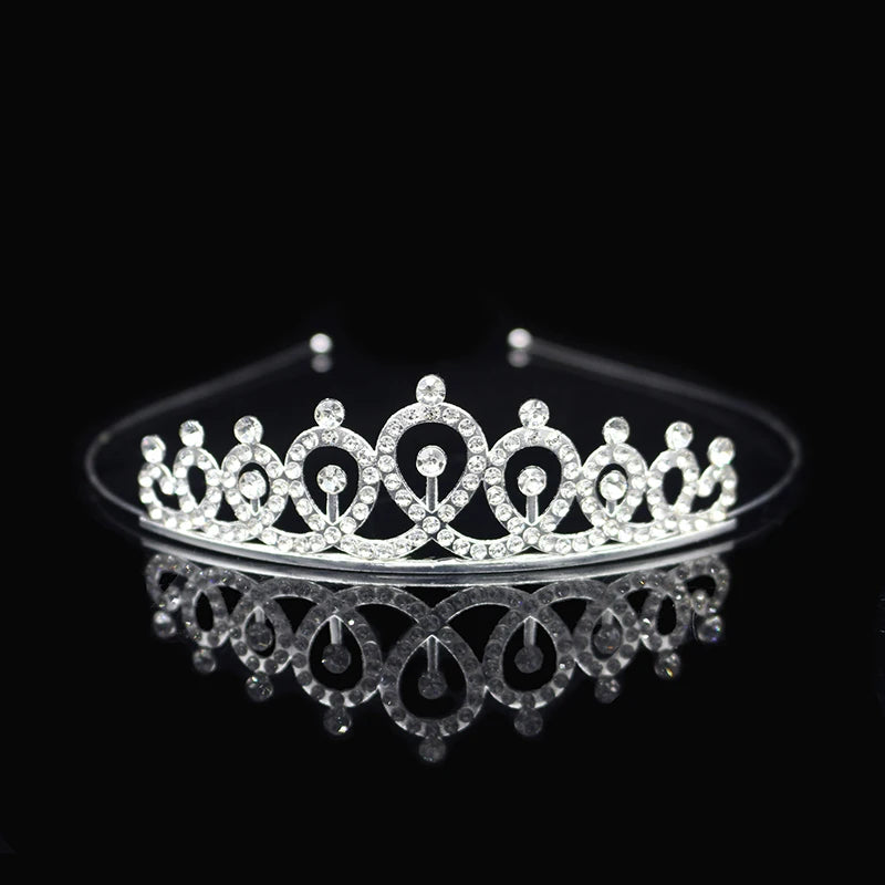Tiara y corona de princesa de cristal brillante para el cabello, exhibidas en una superficie reflectante.