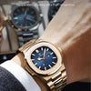 Nahaufnahme einer goldfarbenen Uhr mit blauem Zifferblatt und blauen Zeigern am Handgelenk einer Person.