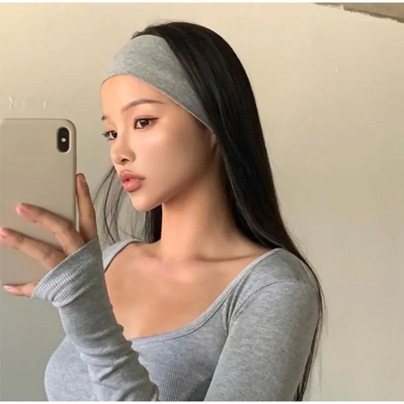 A woman wearing a grey knitted sports headband while holding a smartphone.