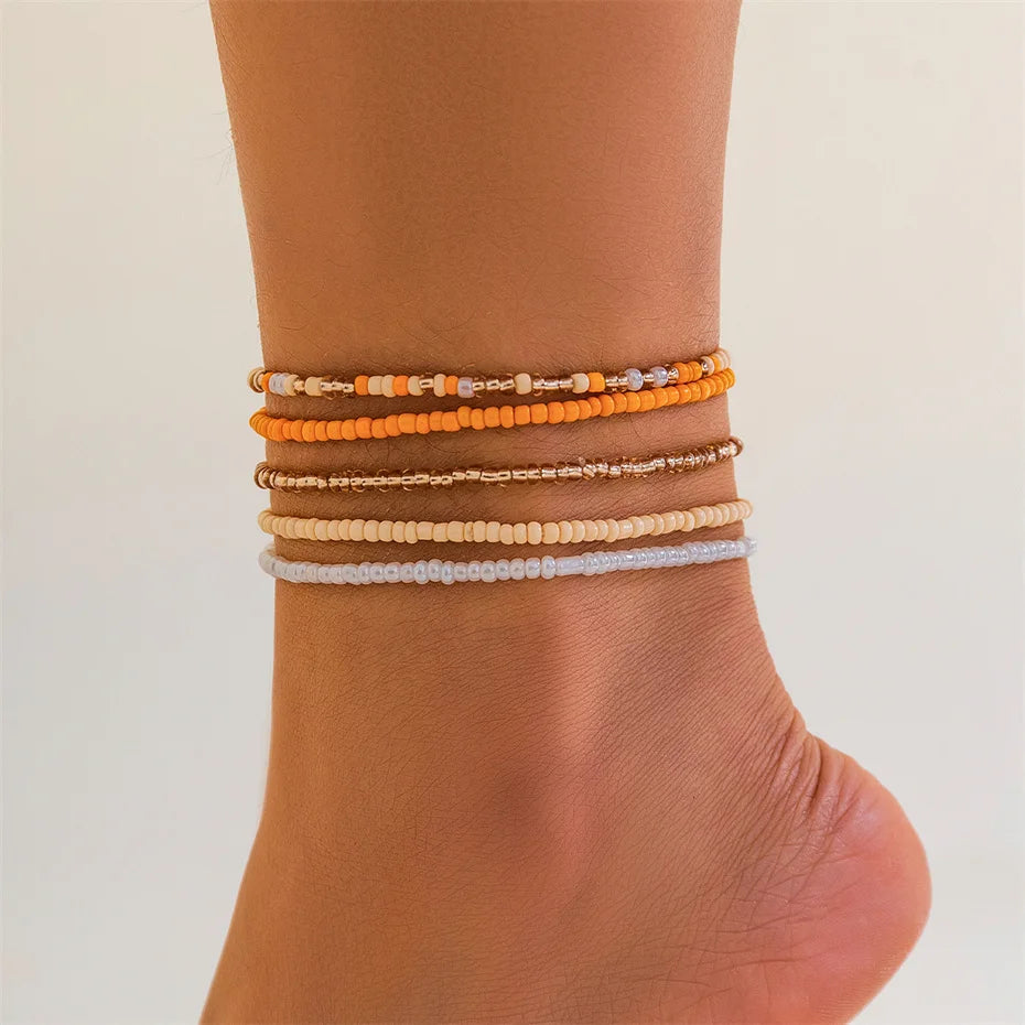 A collection of colorful seed bead anklets and bracelets stacked on a person's ankle.