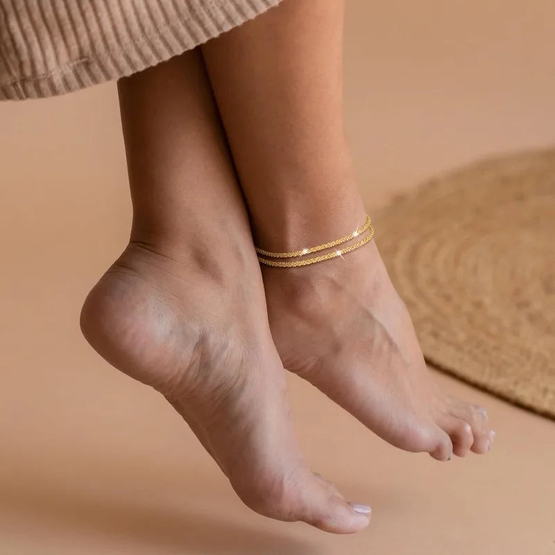 Gold plated glitter layered anklets worn on a person's ankle and foot.