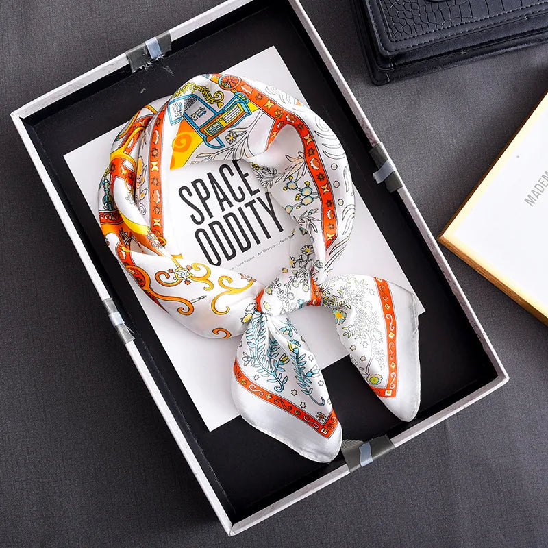 A floral print silk scarf is displayed in a black tray on a dark surface.
