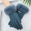 A pair of dark teal plush wrist gloves with fluffy gray faux fur cuffs resting on a white surface.