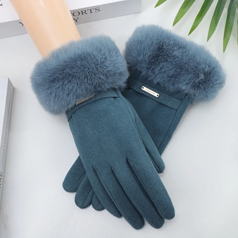 A pair of dark teal plush wrist gloves with fluffy gray faux fur cuffs resting on a white surface.