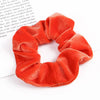 A set of six bright orange velvet scrunchies for hair ties displayed on a white background.
