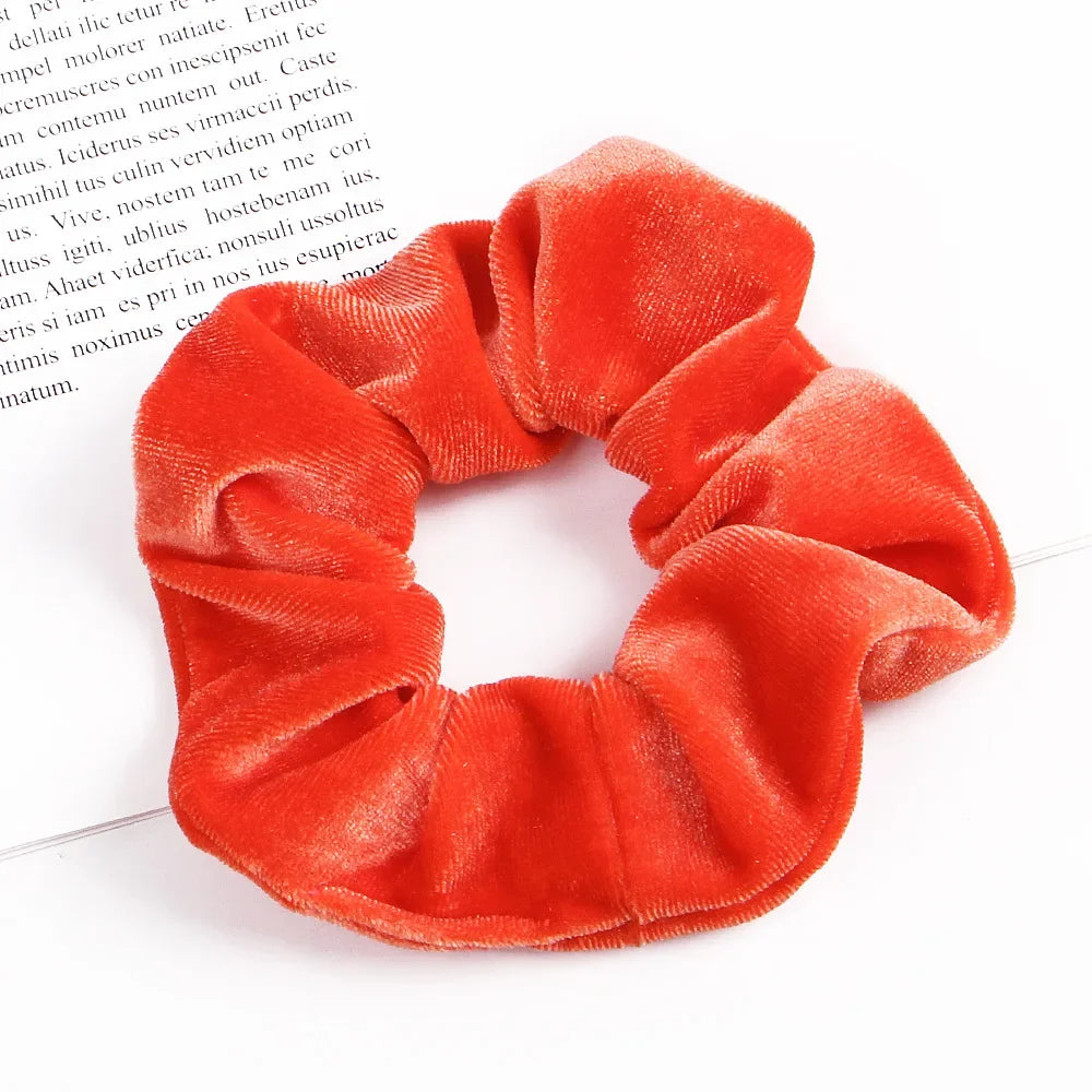 A set of six bright orange velvet scrunchies for hair ties displayed on a white background.
