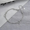 A sterling silver double heart charm bracelet laid on a gray fabric background.