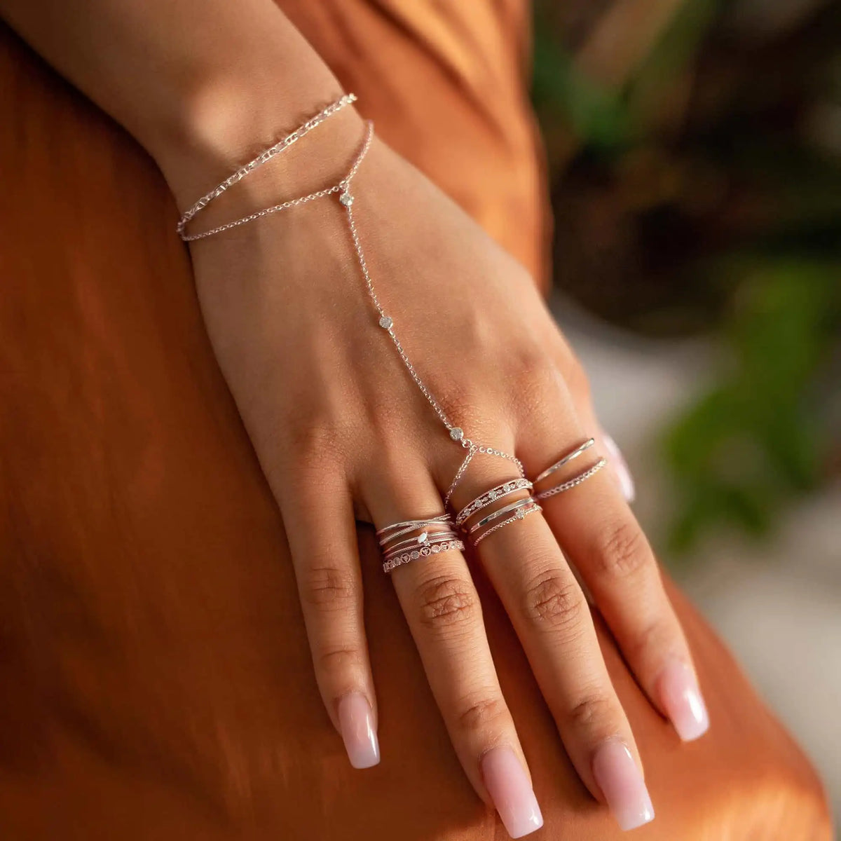 A close-up of a hand wearing a delicate sterling silver geometric bezel charm bracelet on a person's wrist.