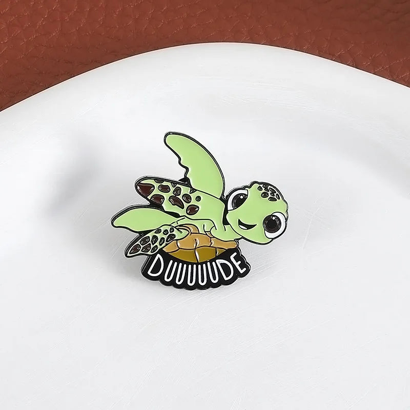A cute sea turtle enamel lapel pin brooch with a green shell and yellow belly, featuring the text DUUUUUDE.