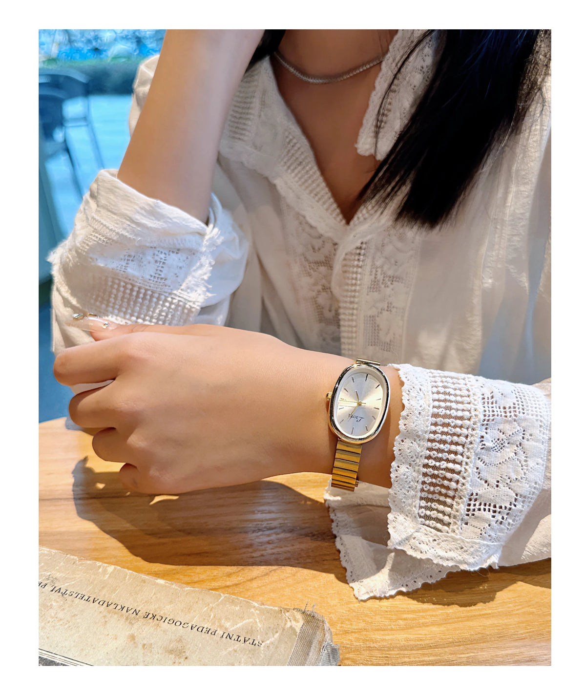Une femme portant une chemise en dentelle blanche et une montre dorée à bracelet en cuir posée sur une surface en bois.