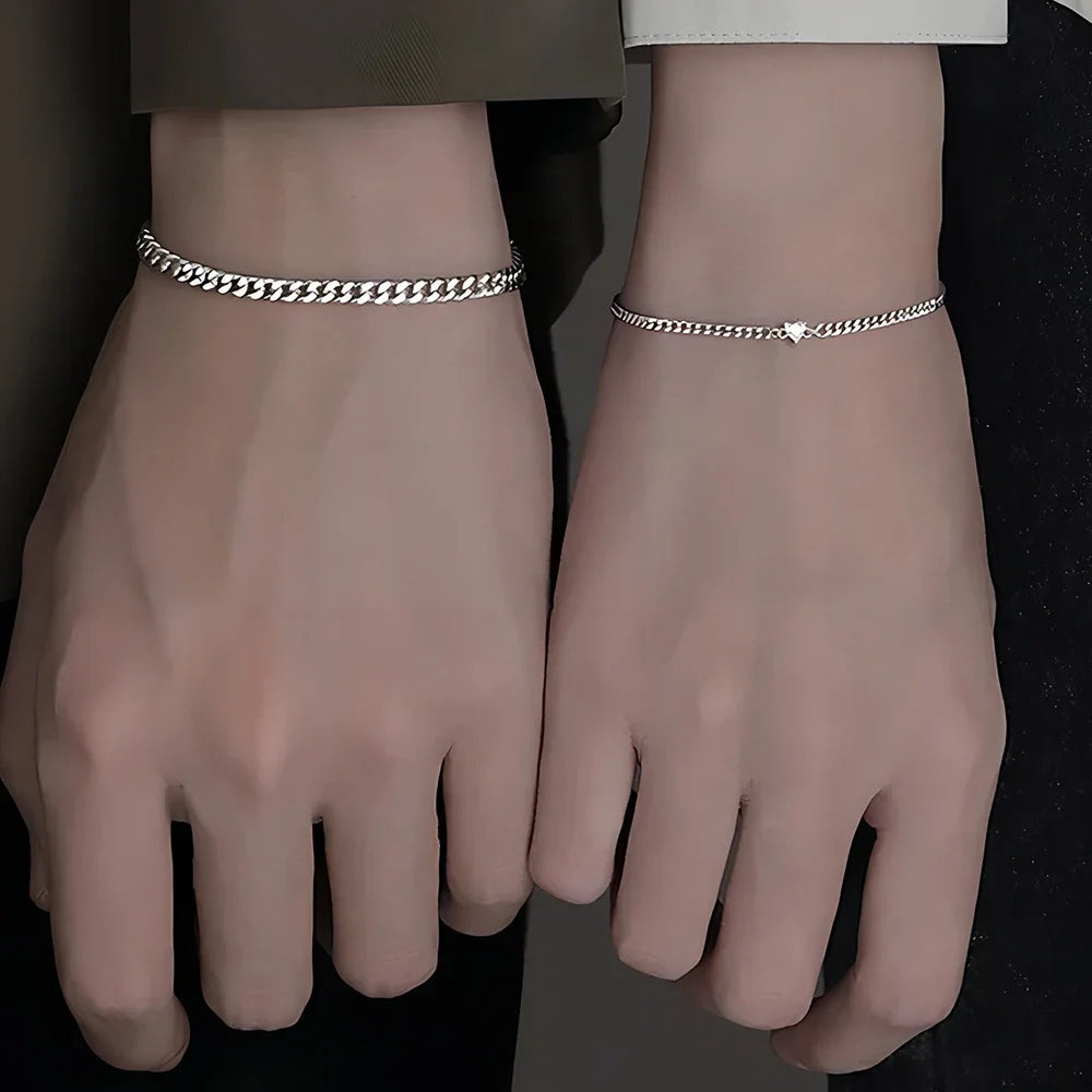 A pair of dainty stainless steel heart link bracelets worn on a person's wrists.