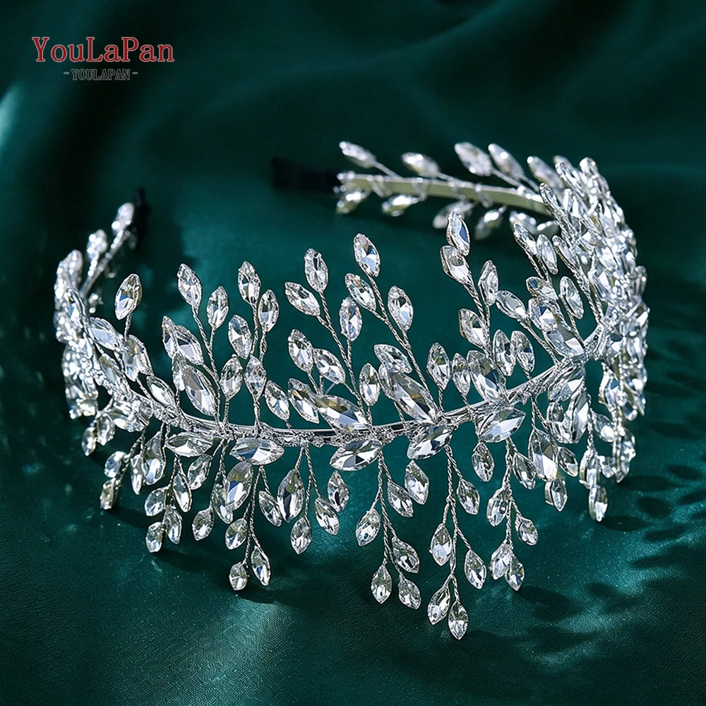 A sparkling silver rhinestone bridal headband with delicate leaves is displayed on a dark green fabric.