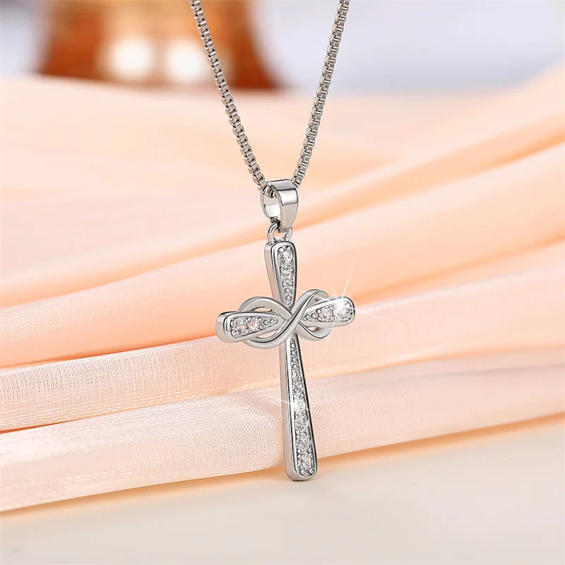 Silver cross pendant necklace with a delicate chain displayed on a pink fabric background