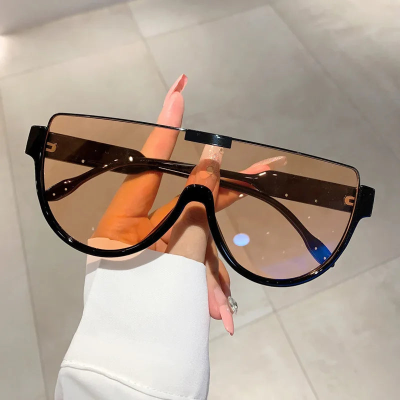 A person is holding a pair of black vintage cat eye sunglasses with brown lenses against a light background.