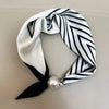 A white and black striped scarf tied in a knot with a pearl magnetic clasp