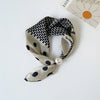 A silk scarf featuring a black geometric print on a beige background tied with a pearl bead.
