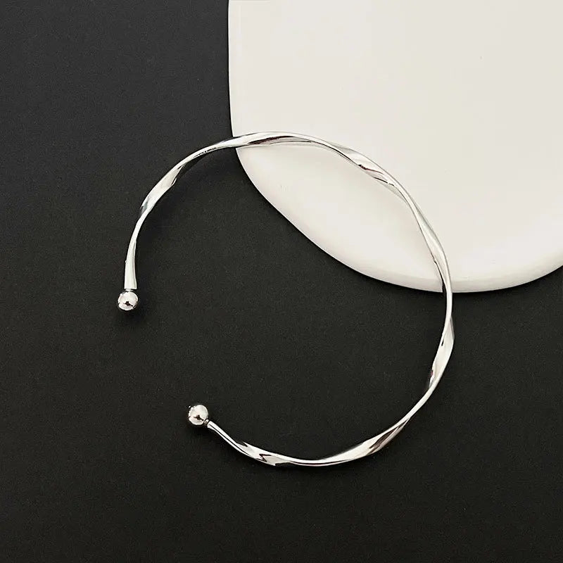 A silver twisted wave cuff bracelet is displayed against a white background on a dark surface.