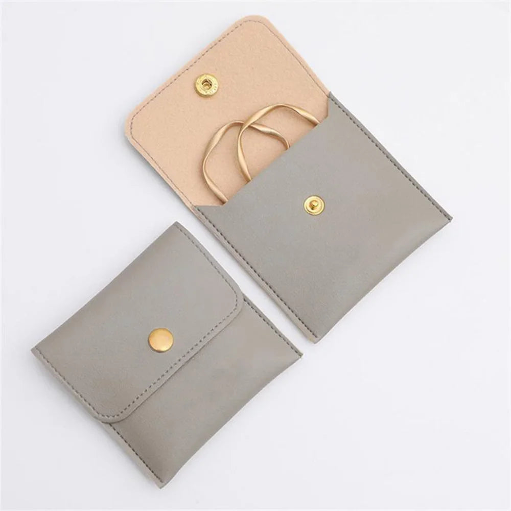 A light beige PU leather jewelry pouch with a snap button and a matching gray version shown diagonally.