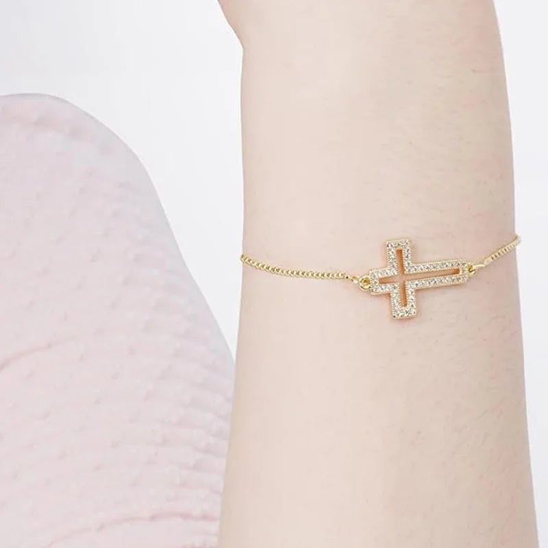 A close-up of an adjustable gold plated cross bracelet with cubic zirconia worn on a wrist.