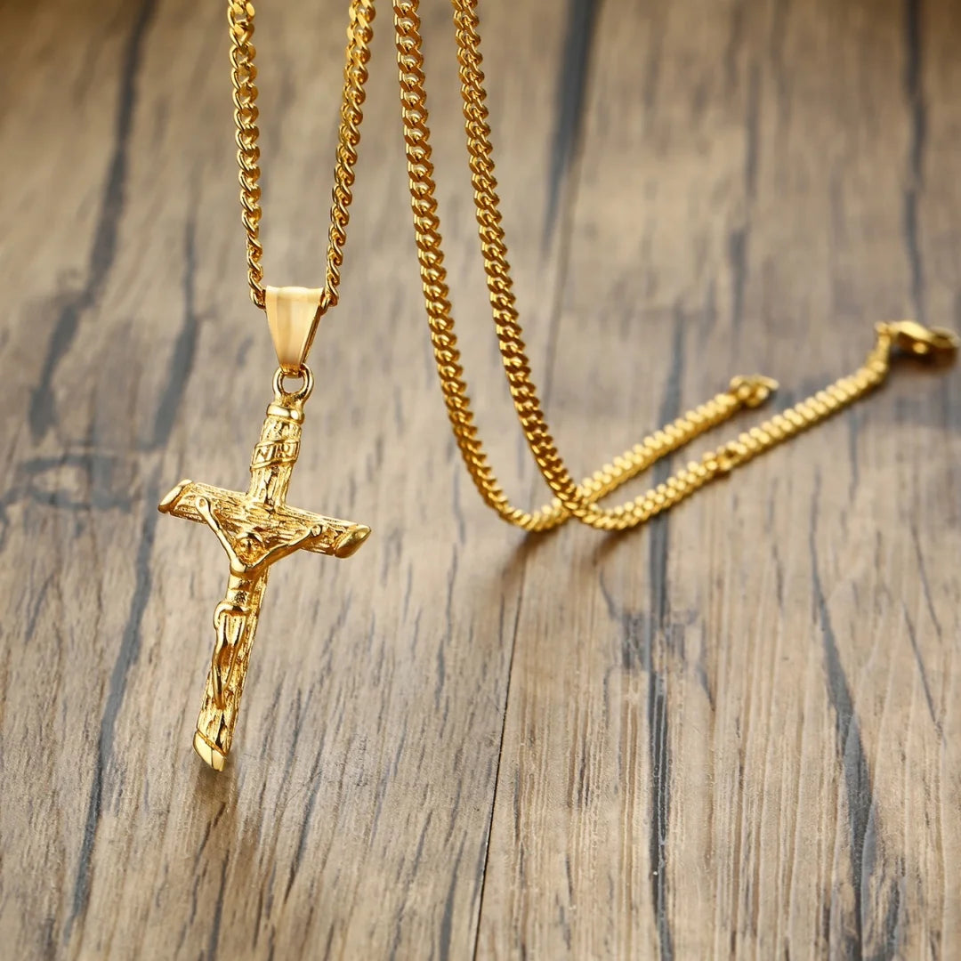 A gold-finished stainless steel cross necklace with a chain and a pendant lying on a wooden surface.