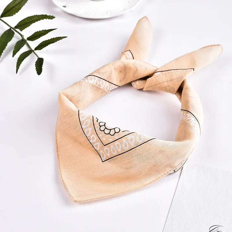 A beige bandana headband and wrist wrap set with black embroidered patterns on a white surface.