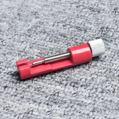 A set of three precision watch link pin remover tools with red and silver components resting on a gray textured surface.