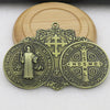 A brass Saint Benedict protection medal featuring a figure and Latin inscriptions, set against a light wooden background.