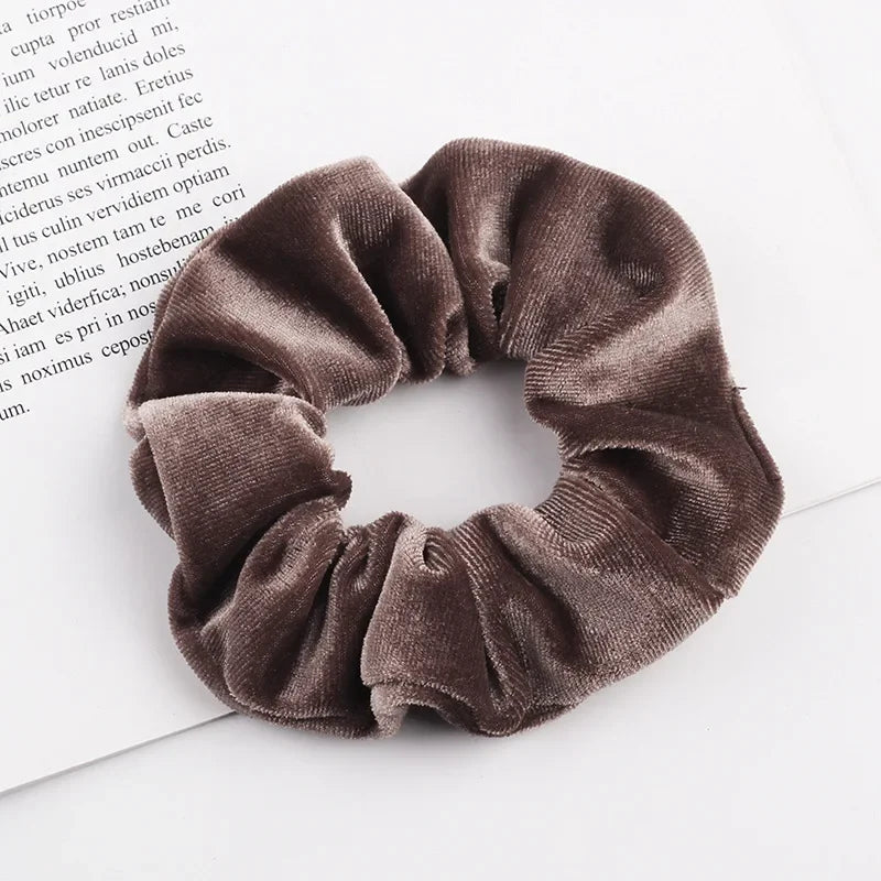 A close-up of a dark brown velvet scrunchie with gathered fabric texture resting on a white background.