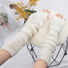 A pair of cream-colored knitted fingerless gloves displayed on a black wire stand.