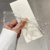 A hand holds a pair of clear, large square anti-blue light spectacles against a white background.