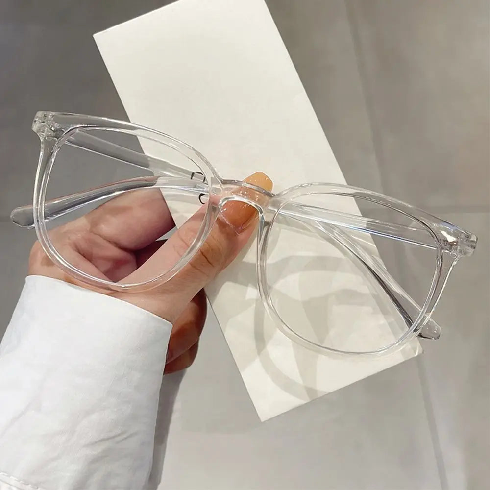 A hand holds a pair of clear, large square anti-blue light spectacles against a white background.