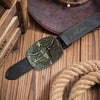 Cinturón de cuero negro con diseño western grabado y hebilla decorativa sobre una superficie de madera.