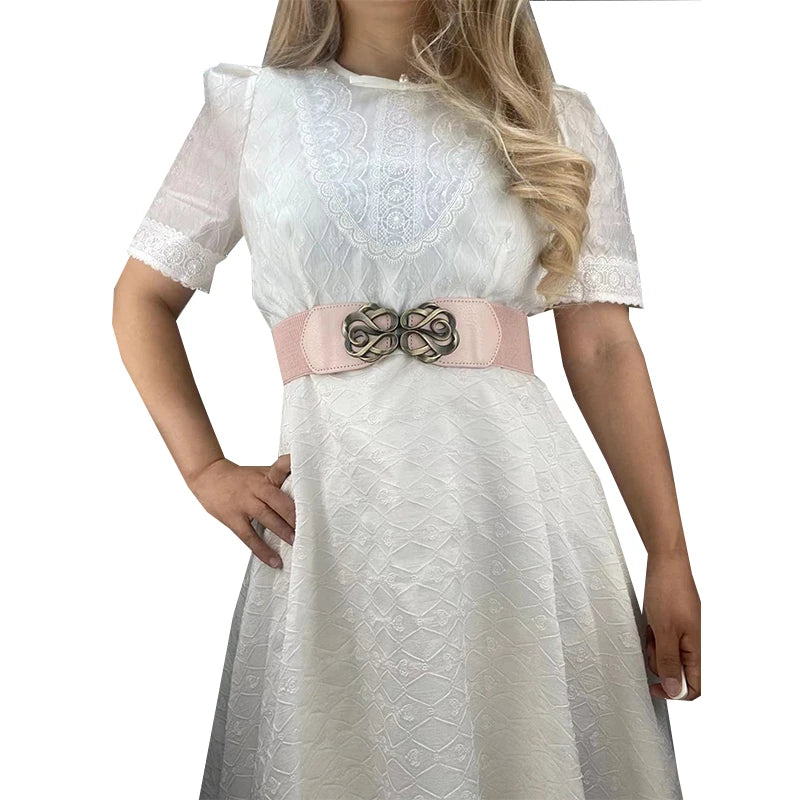 White lace-trimmed dress with sheer sleeves and a light pink elastic belt featuring a brass buckle