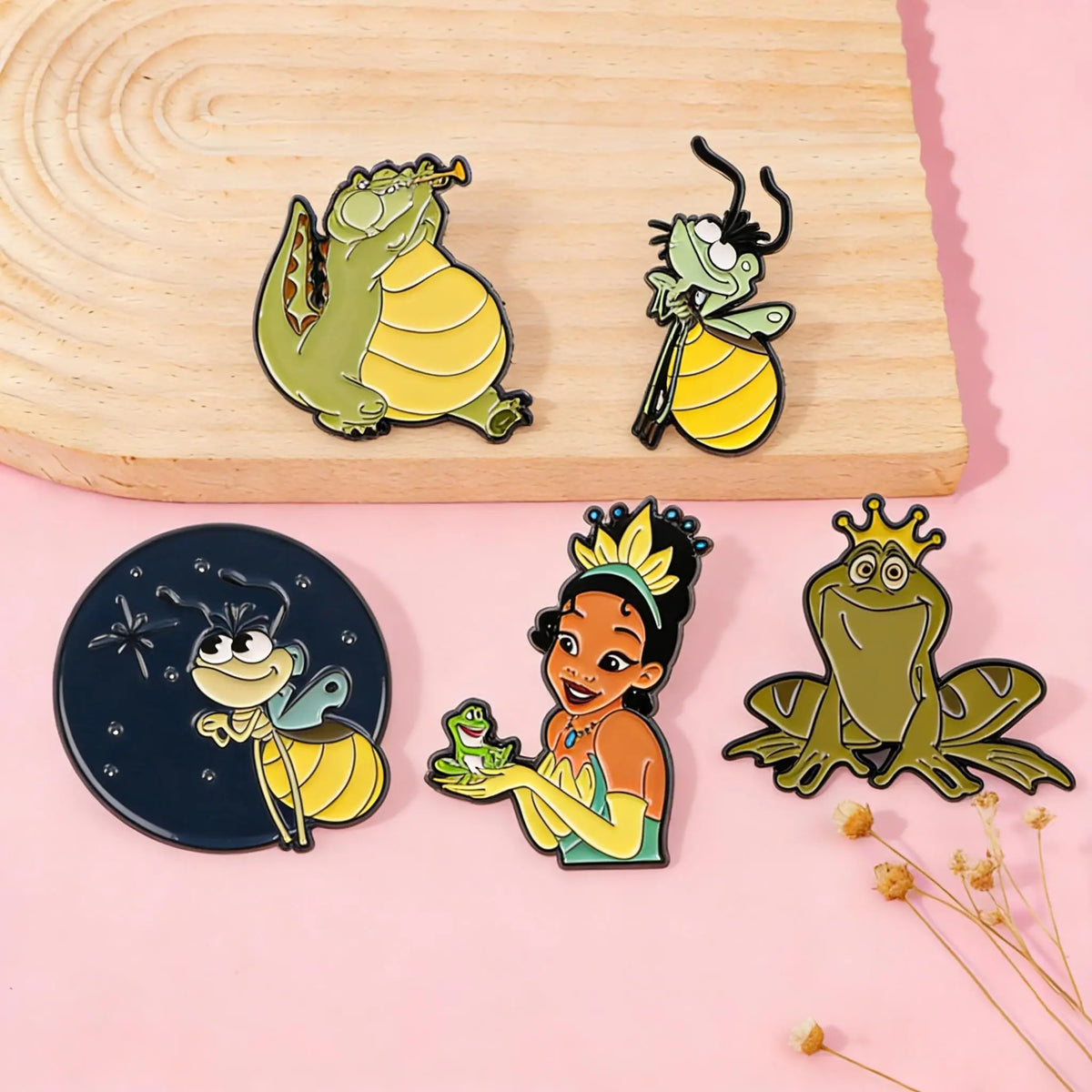 A collection of enamel pins featuring cute firefly and frog characters on a pink background.