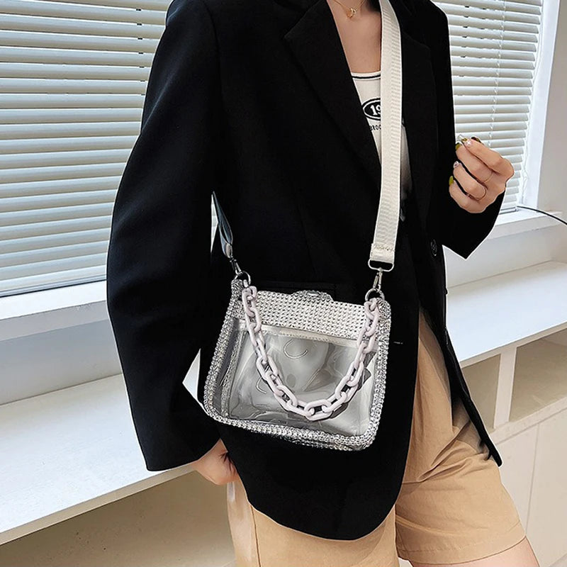 Una persona con blazer negro y pantalones caqui sostiene un bolso cruz de PVC transparente.
