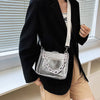 Una persona con blazer negro y pantalones color arena sostiene un bolso cruz transparente de PVC.