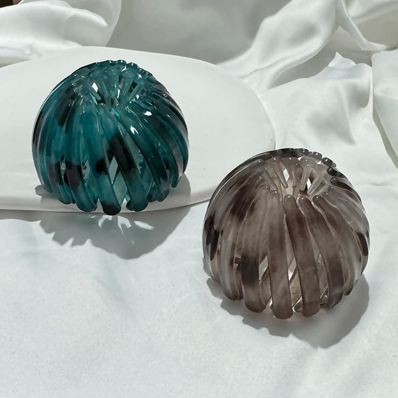 Two elegant glass horsetail hair clips, one teal and one smoky gray, resting on a white plate.