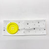 A white headband decorated with silver stars and small dots, featuring a bright yellow button.