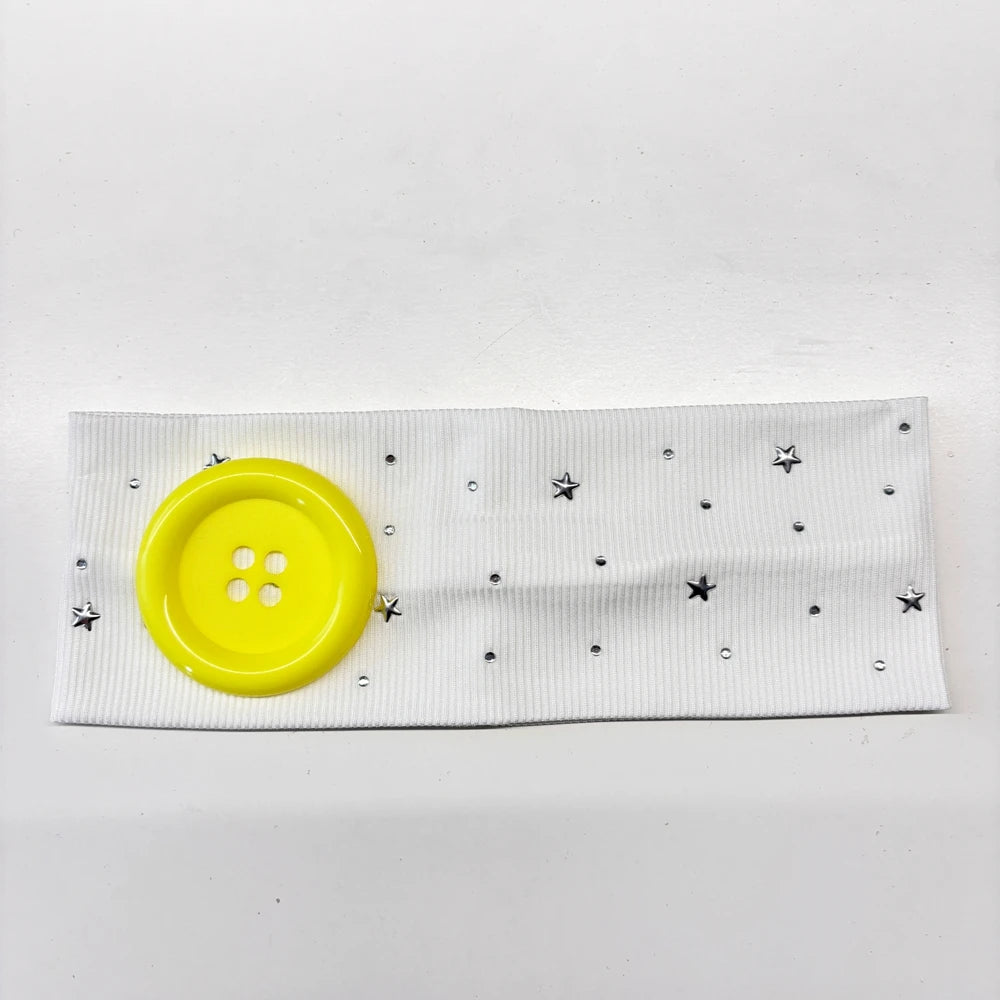 A white headband decorated with silver stars and small dots, featuring a bright yellow button.