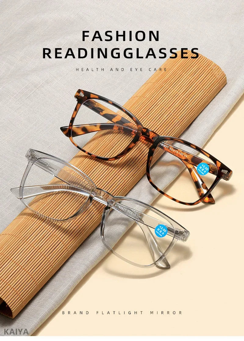 Un par de gafas de lectura color tortuga descansando sobre una superficie de bambú con un fondo de tela gris claro.