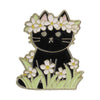 A black cat enamel brooch featuring white and pink flowers and green foliage.