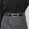 A close-up of a black blouse and gray trousers featuring a black leather belt with a gold buckle.