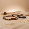 A close-up of a brown skinny leather belt with a gold buckle resting on a beige fabric.