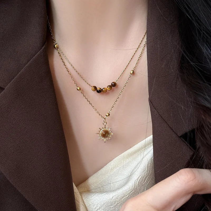 Gold-toned necklace featuring a tiger eye sunflower pendant worn against a brown blazer.