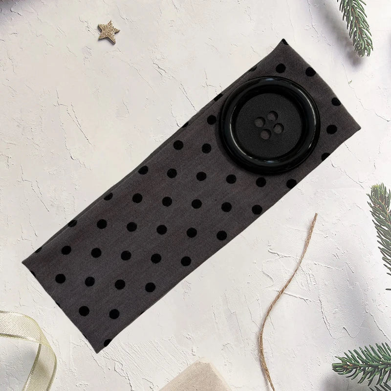 A black polka dot fabric headband lying on a white surface with a small star and pine sprig nearby.