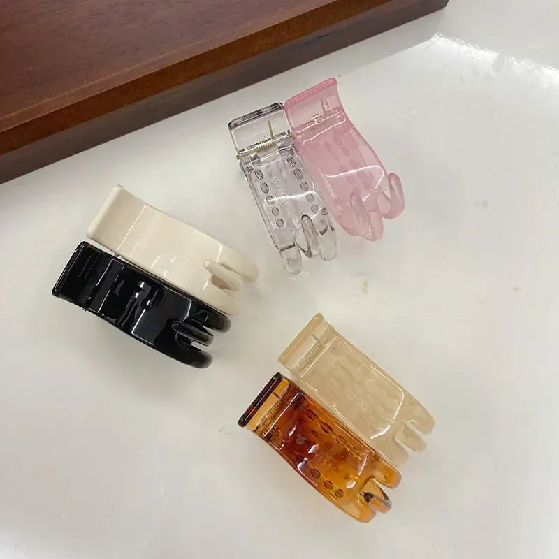 Several transparent acrylic hair claws in pink, beige, and black are displayed on a white surface.
